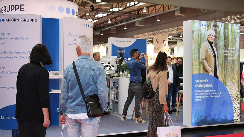 Das Bild zeigt den Messestand der Ahorn Gruppe mit Menschen davor, die den Stand betrachten 