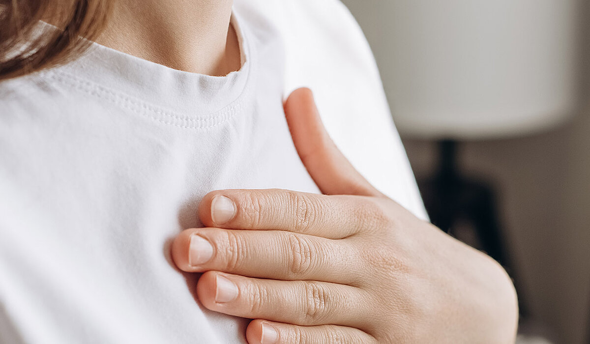 Frau fasst sich mit der Hand auf die Brust
